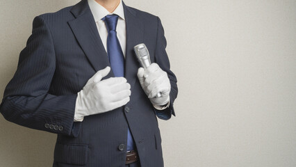 白い手袋でマイクを持つ・スーツを着た男性