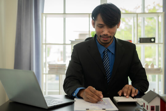 Black male real estate agent puts a miniature model of a house on a table inside a real estate sales office. home buying ideas from real estate agents