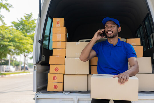 Young black male courier happy delivery with technology, tracking and courier service concept. A truck full of cardboard boxes in hand delivers a parcel to a man in a business district.
