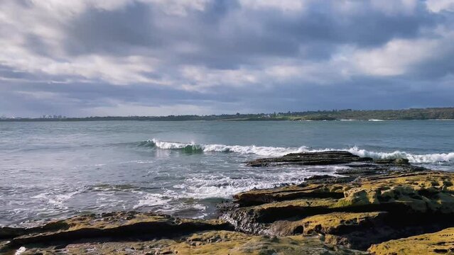 HD Video-Panning view at the entry to Botany Bay in Sydney Metropolitan area with waves splashing on the rocky beach at Kurnell in the foreground, and La Perouse hills in the background-NSW, Australia