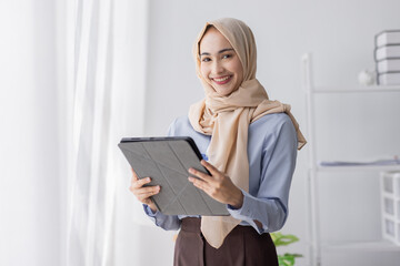 Young business Asian Business muslim woman in purple hijab using tablet and phone, standing near the window in workplace business finance concept.	