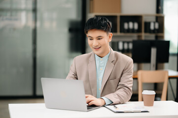 Fototapeta premium Young Asian business man working at office with laptop, tablet and taking notes on the paper.