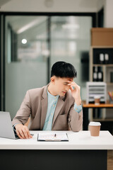 Frustrated young businessman working on a laptop computer sitting at his working place in office
