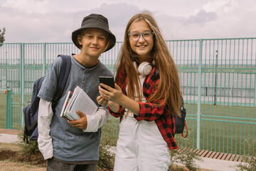 teenage boy and girl outdoors portrait, communicating and looking at smartphone