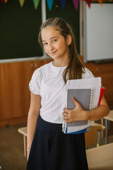 cute smiling teenage girl posing with copybooks at classroom
