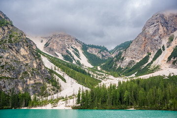 Fototapeta na wymiar Braies lake surrounded by pine forests and the rocky ranges of the Dolomites in cloudy day, Italy.