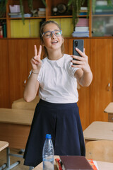 cute smiling teenage girl posing with smartphone at classroom