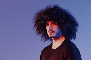 Portrait of a stylish man with curly hair in smoke on a blue background multinational, color light, trendy, modern concept.