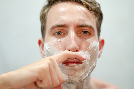 Handsome caucasian man pretending to have a mustache with his finger in front of the mirror. Movember concept. No shave november. - Powered by Adobe