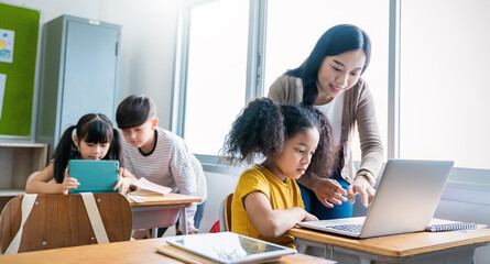 Pupil black girl learn computer teacher in classroom at elementary school. Student girl studying in primary school. Children writing notes in classroom. Education knowledge online digital technology