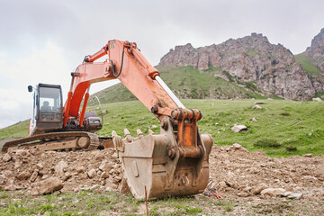 Excavator works in the highlands. Clears the consequences of a mudslide in the gorge of the mountains. repair and expansion of a road
