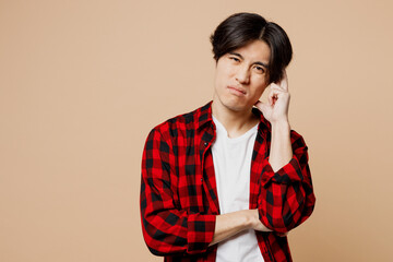 Young thoughtful upset sad man of Asian ethnicity he wear red checkered shirt casual clothes look...