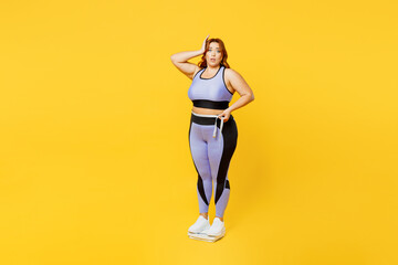 Full body young plus size big fat fit woman wear blue top warm up training stand on scales check result look at measure tape isolated on plain yellow background studio home gym. Workout sport concept.