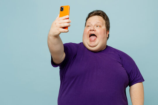 Young cool chubby overweight man wear purple t-shirt casual clothes do selfie shot on mobile cell phone post on social network isolated on plain pastel light blue cyan background. Lifestyle concept.