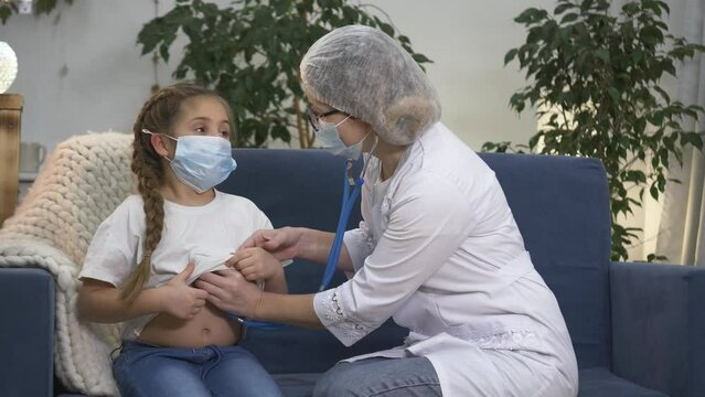 woman pediatrician examines child girl with stethoscope.little patient at doctor at clinic.Pediatrician examining sick child wearing face mask. Coronavirus pandemic. Virus prevention.children's doctor