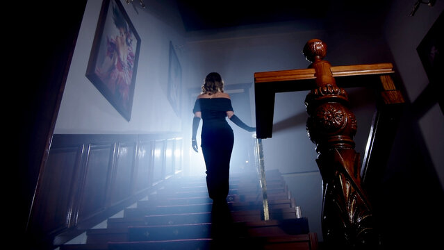 Beauty And Form. The Silhouette Of A Beautiful, Young Woman Against A Dark Background Is Climbing Up The Old Stairs.