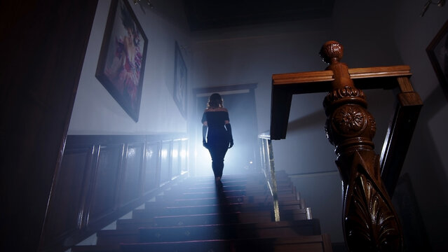 Beauty and form. The silhouette of a beautiful, young woman against a dark background is climbing up the old stairs.