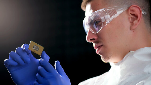 Close up portrait of a young computer engineer with a microchip.Engineer man in sterile suit is holding Microchip with symbols in modern design factory , futuristic and artificial intelligence concept
