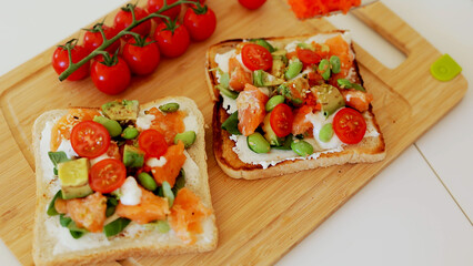 Breakfast toast with cream cheese, salmon and avocado and cherry tomatoes. the concept of healthy eating and healthy lifestyle. cooking sandwiches with fillet of red fish.