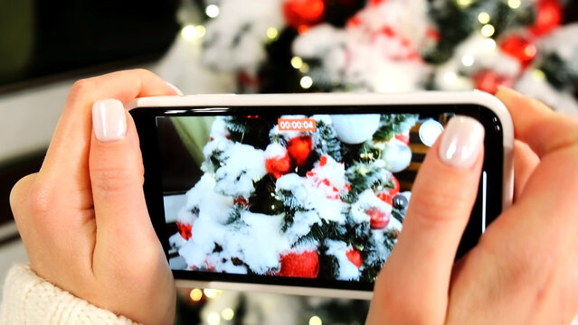 A man takes pictures on a smartphone of a Christmas tree with gifts with a New Year's background