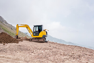 Obraz premium Excavator works in the highlands. Makes a trench for communications. water and electricity. in the gorge of the mountains. repair and expansion of a road