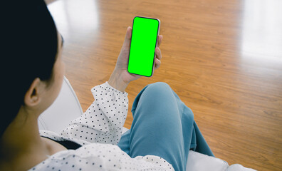 Mockup image of asian woman holding black smartphone with blank green screen at home.