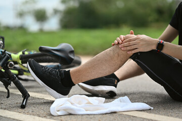 Man cyclist with injured knee sitting near bicycle outdoors, falling down from bicycle. Concept...