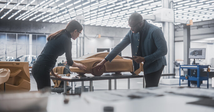 Young Apprentice Car Modeler Advising with Senior Automotive Designer on Creating a 3D Polymer Clay Model of a Modern Electric Car. Team of Diverse Specialists Working in Creative Agency - Powered by Adobe
