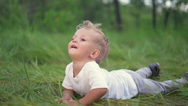 Joyful happy boy crawling in park. First steps. The boy crawls in forest park on the grass. Boy dream concept. The kid takes the first steps in the park on the green grass. Happiness and fun concept