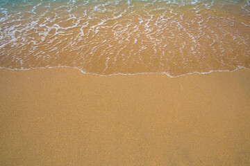 Soft blue ocean wave on clean sandy beach.