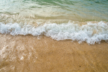 Soft blue ocean wave on clean sandy beach.