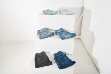 six pairs of different jeans lie on a white podium. minimalist clothing exhibition