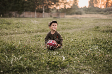Naklejka na ściany i meble A boy is playing with a soccer ball in the fresh air in the countryside. The boy's sincere smile. Childhood in the fresh air.