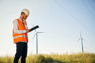 In orange colored uniform. Service engineer is on the field with windmills