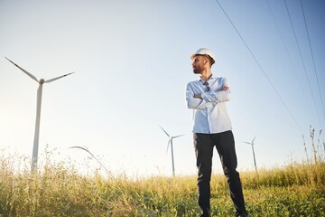 Handsome service engineer is standing on the field with windmills