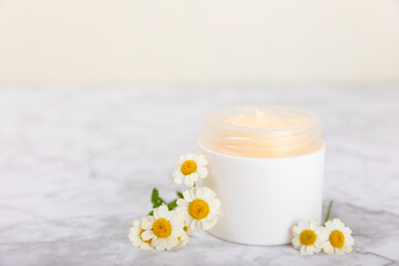 Obraz na płótnie Canvas Open jar of moisturizing cream for face, body and hands with a chamomile flower on a light background. Herbal dermatological cosmetic hygiene cream. Natural cosmetic product. Beauty concept. MOCKUP