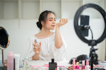 An attractive Asian female beauty blogger influencer is trying a new perfume in her video