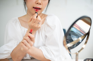 Close-up image of a pretty Asian female applies lipstick on her lips, doing her daily makeup.