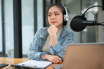A beautiful and thoughtful Asian female radio host sits at her desk in her studio