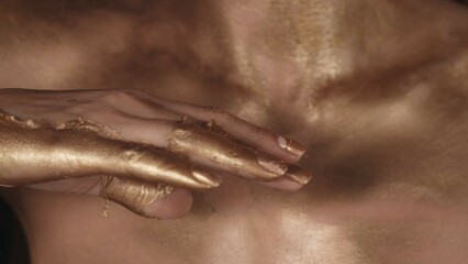 Closeup camera shot of the woman hands and body covered in dried golden paint