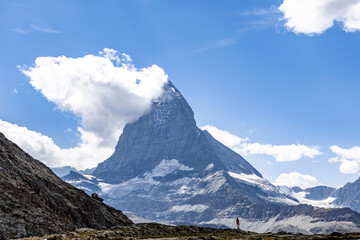 Matterhorn with a cloud around the top and a woman in a red dress in the foreground