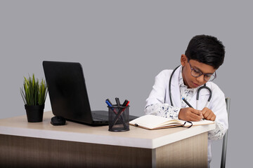 Portrait Indian Asian kid boy aged 7 to 8, wearing a doctor apron with stethoscope. with laptop...