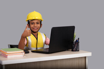 Indian Asian kid boy aged 7 to 8, wearing a yellow helmet and Safety jacket. with laptop showing Thumbs up. He had a dream to future study as an engineer. He smiled happily, Concept little engineer