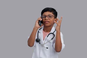 Indian Asian kid boy aged 7 to 8, wearing a doctor apron with stethoscope. talking on smartphone. He had a dream to future study as Doctor. He smiled happily, Concept little Doctor