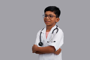 Indian Asian kid boy aged 7 to 8, wearing a doctor apron with stethoscope. standing and folding both hands. He had a dream to future study as Doctor. He smiled happily, Concept little Doctor
