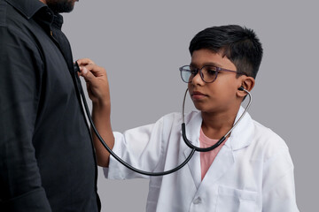 Indian Asian kid boy aged 7 to 8, wearing a doctor apron with stethoscope. checking heartbeat of...