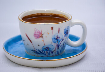 white and blue Cup of Turkish Coffee on a blue plate and gold plated tea spoon , flowers and...