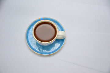 white and blue Cup of Turkish Coffee on a blue plate and gold plated tea spoon , flowers and butterfly on the ceramic mug 