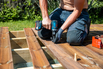 Deck construction, builder hand with electric screwdriver installing impregnated wooden boards