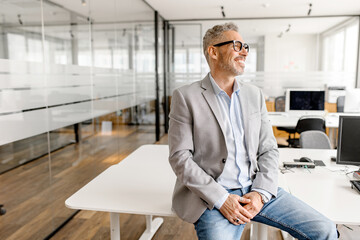 Serene modern middle aged businessman in formal wear leaned on the desk looking away, inspired and calm mature business owner at the office, confident grey-haired man in relaxed pose - obrazy, fototapety, plakaty